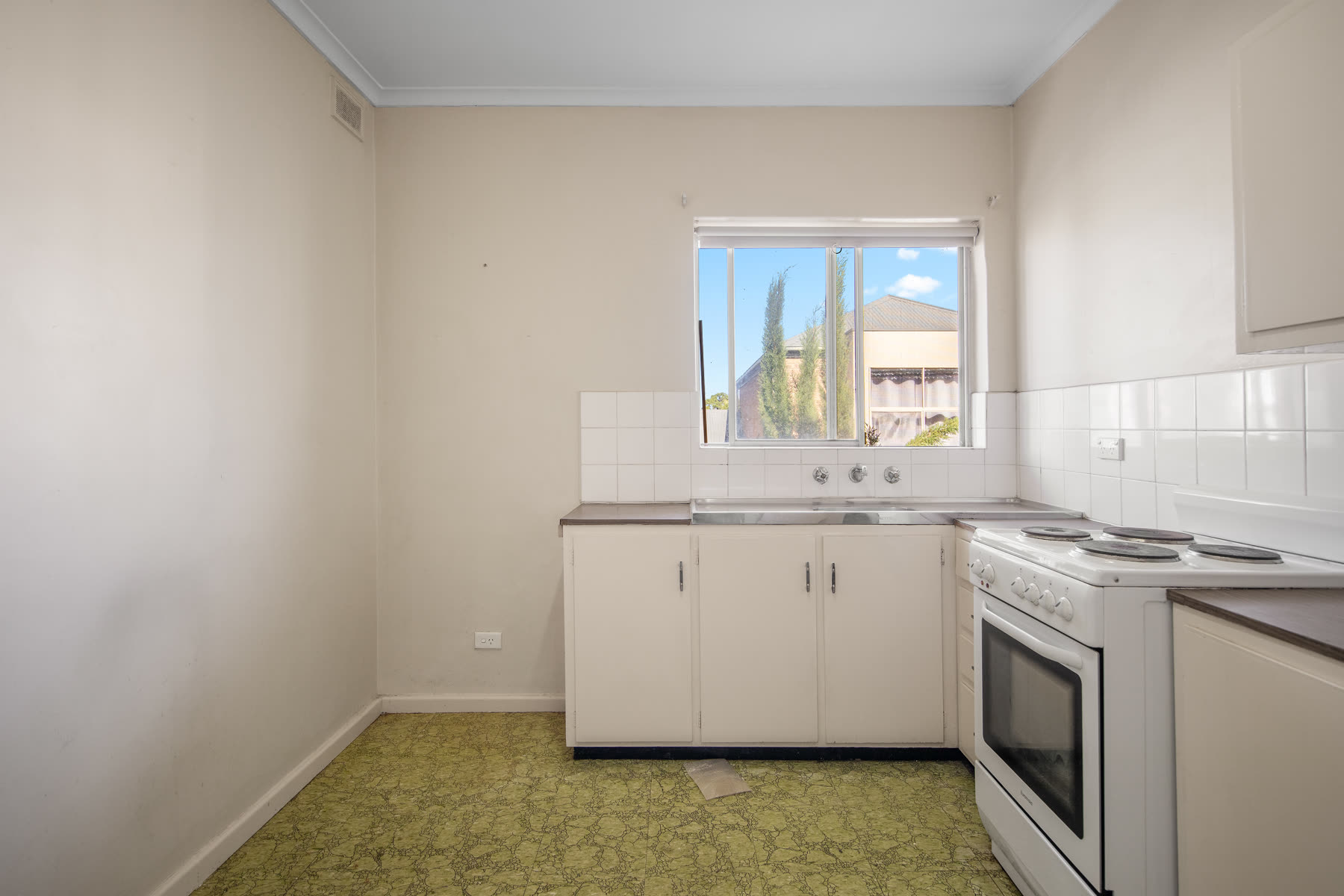 Dated cream kitchen with green patterned flooring before renovation